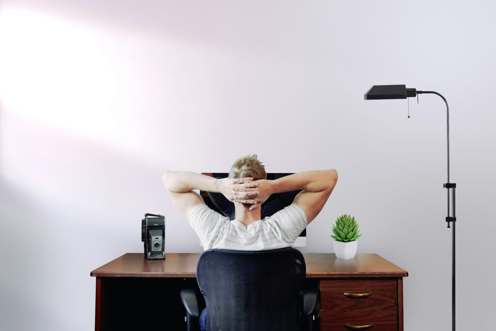 man holding his head while sitting on chair near computer desk trying to decide which MiniStays cancellation policy to choose